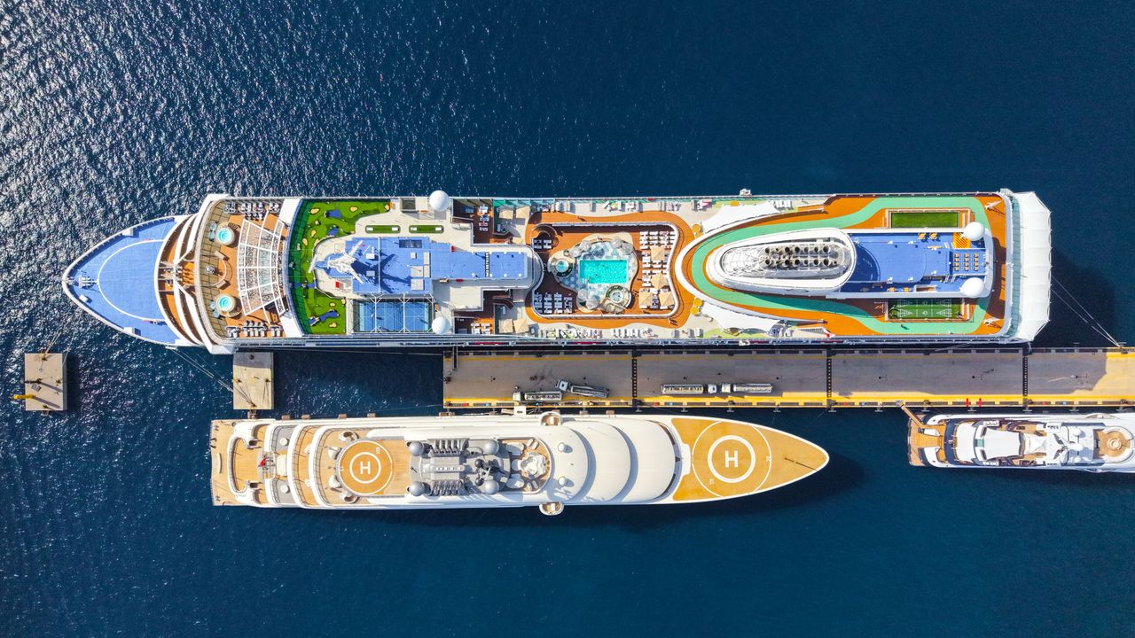 Top-down view of two luxurious cruise ships moored at a sunny port, showcasing pools and helipads.