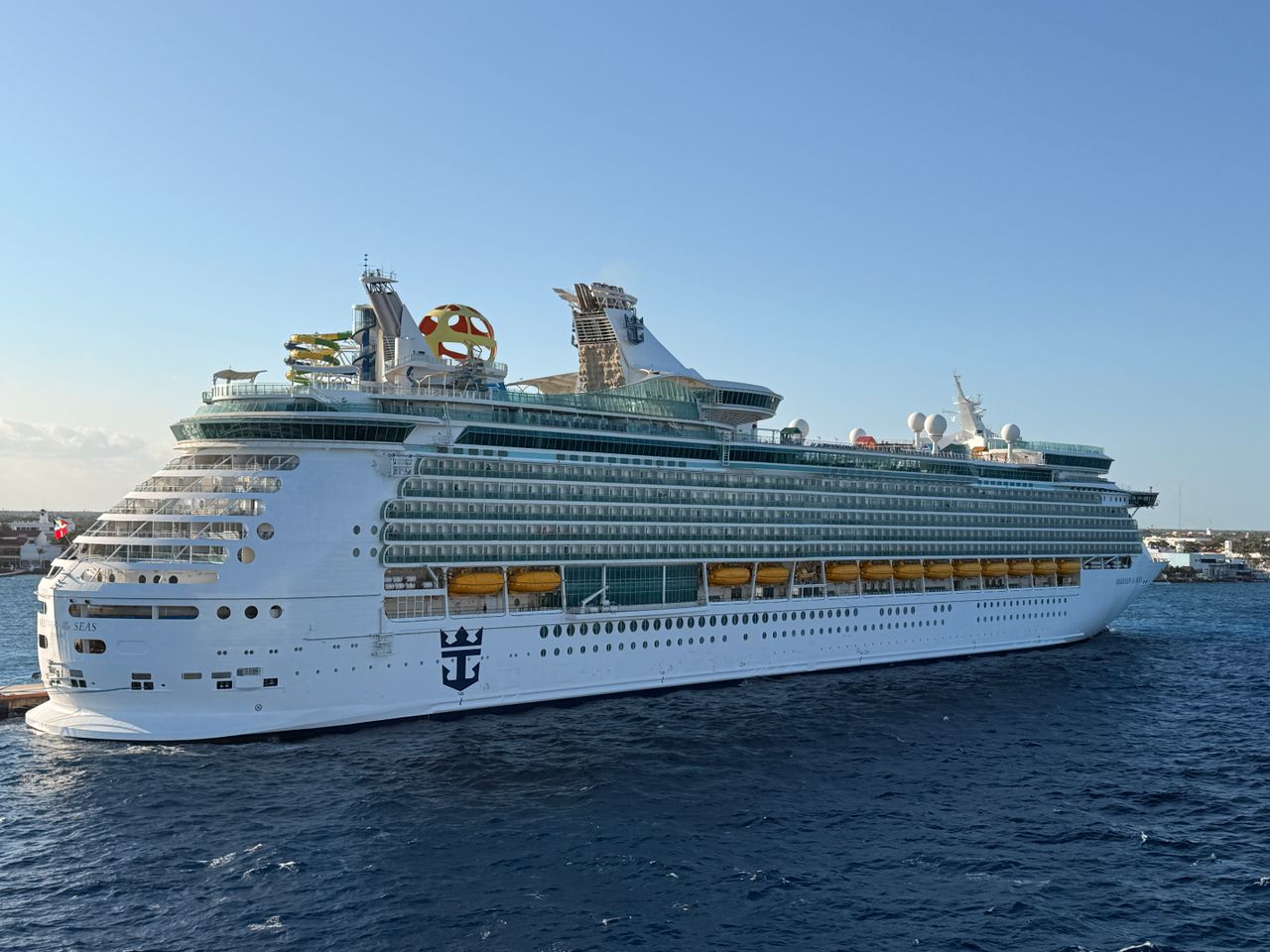 Luxurious cruise ship docked in a sunny harbor showcasing its grandeur with blue ocean backdrop.