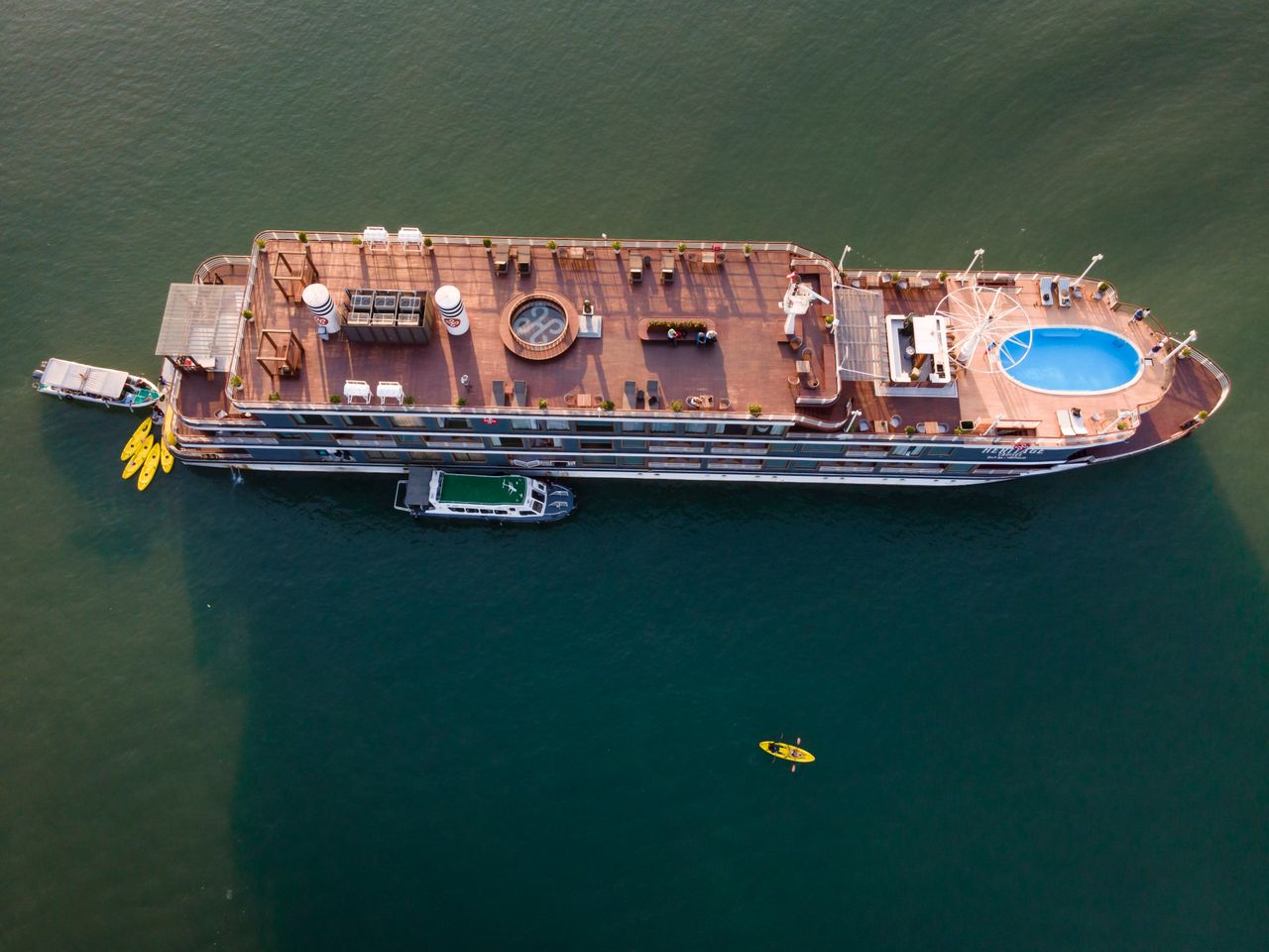 Drone shot capturing a luxurious cruise ship sailing in clear waters, complete with a pool and kayaks.