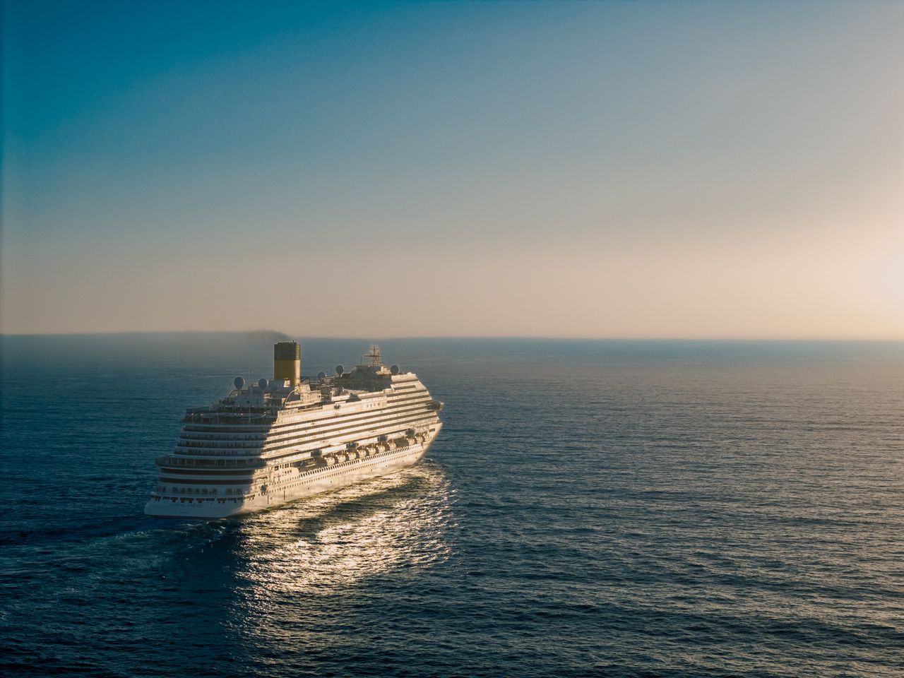 Services-02 A cruise ship gracefully sails across the ocean at sunset, creating a tranquil scene.
