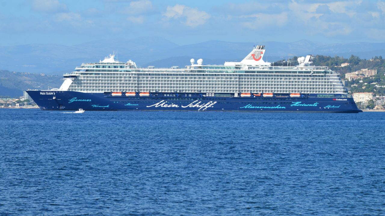 creative A luxury cruise ship named Mein Schiff sails across the ocean under a clear blue sky.
